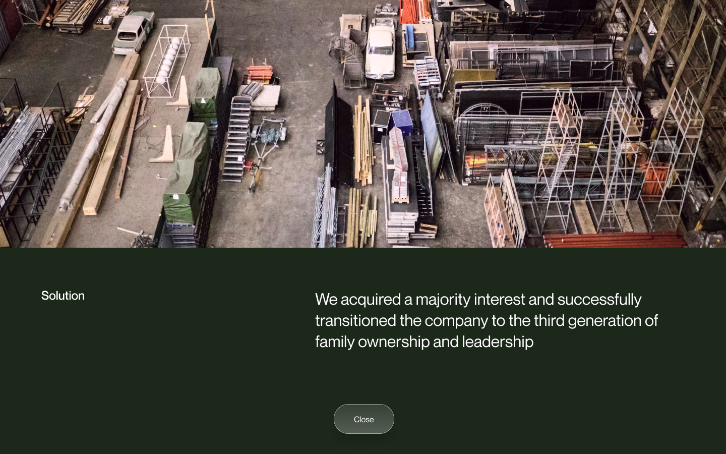 Overhead view of an industrial warehouse with various stacked metal frames, wooden planks, and a white vintage car parked inside.